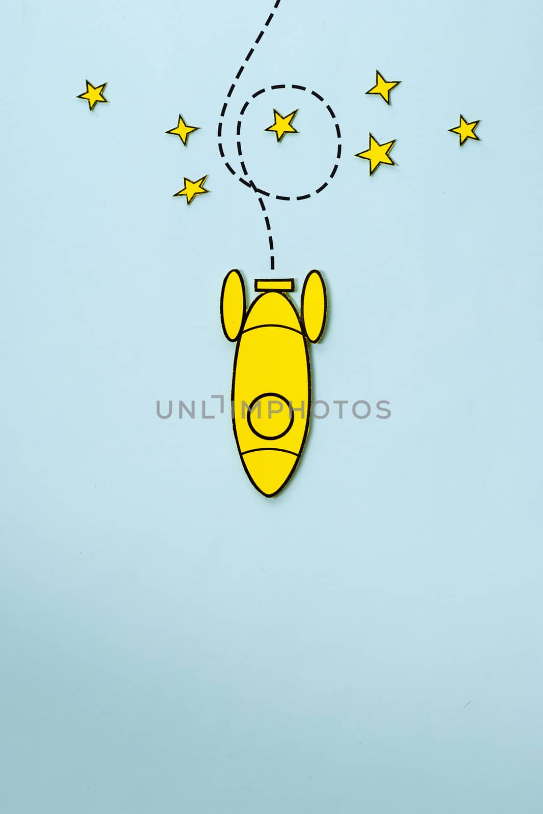Little yellow rocket looping around stars on its way back to earth over a blue background with copy space