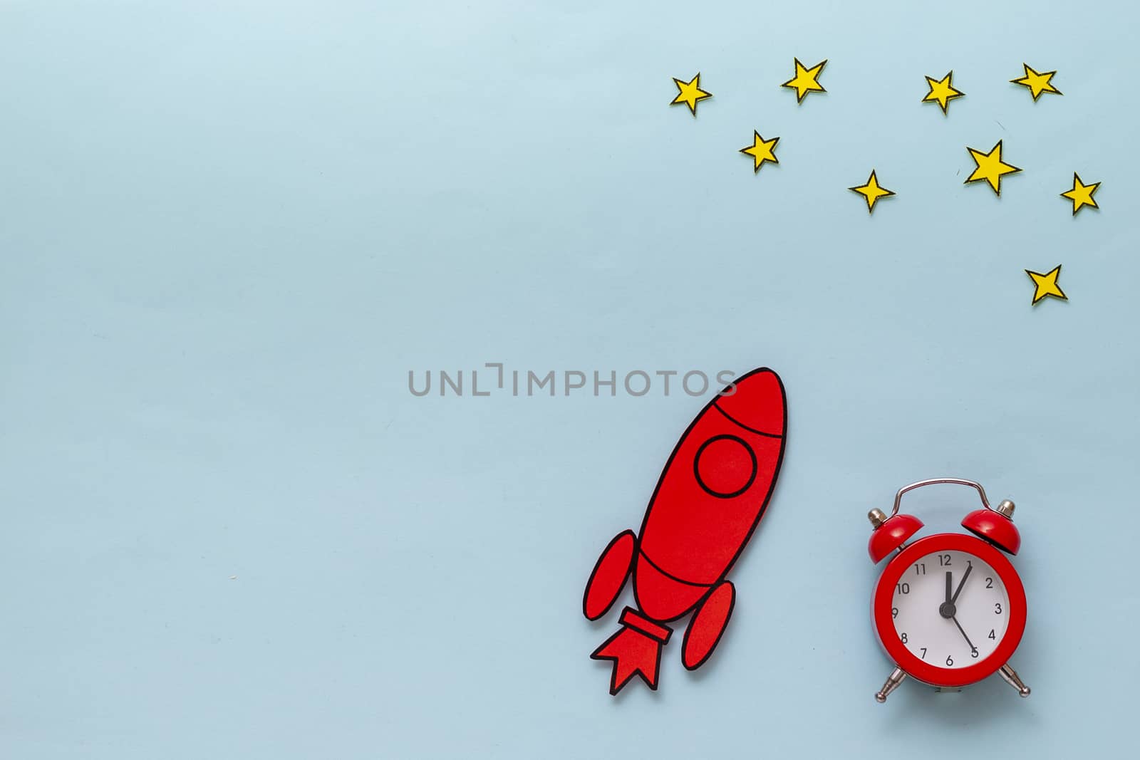Red cartoon rocket with alarm clock and yellow stars in a conceptual image on a blue background with copy space