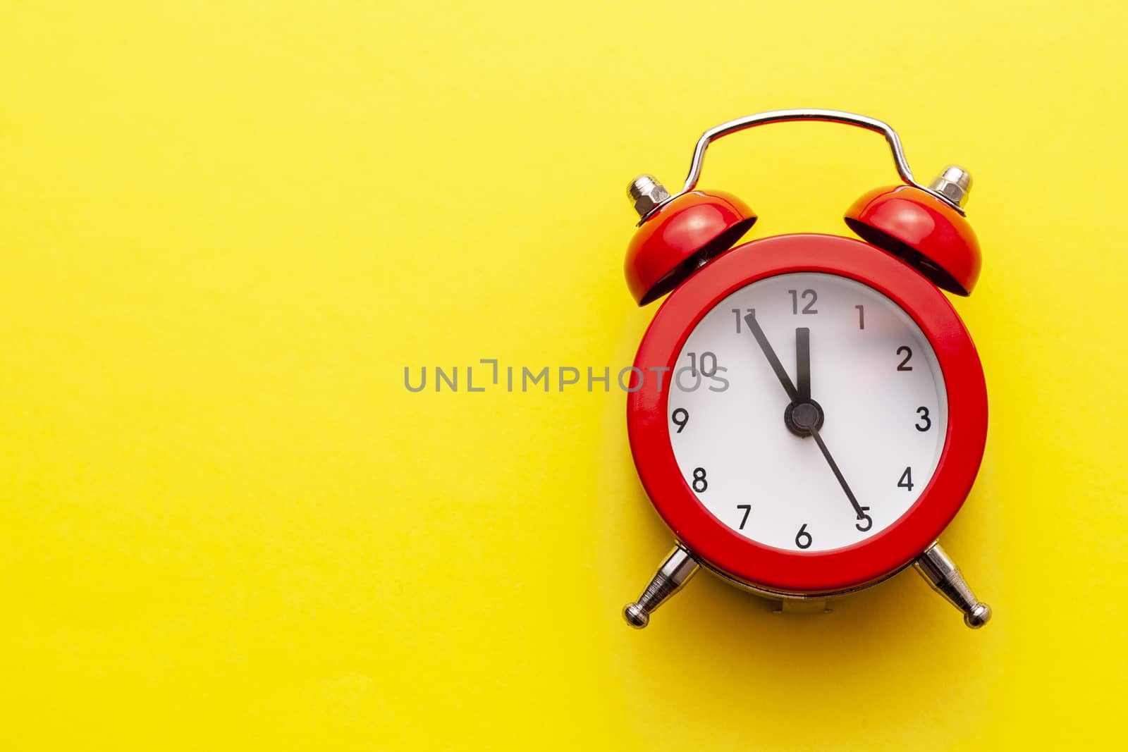 Colorful red traditional alarm clock with bells on a bright yellow background with copy space placed to the side