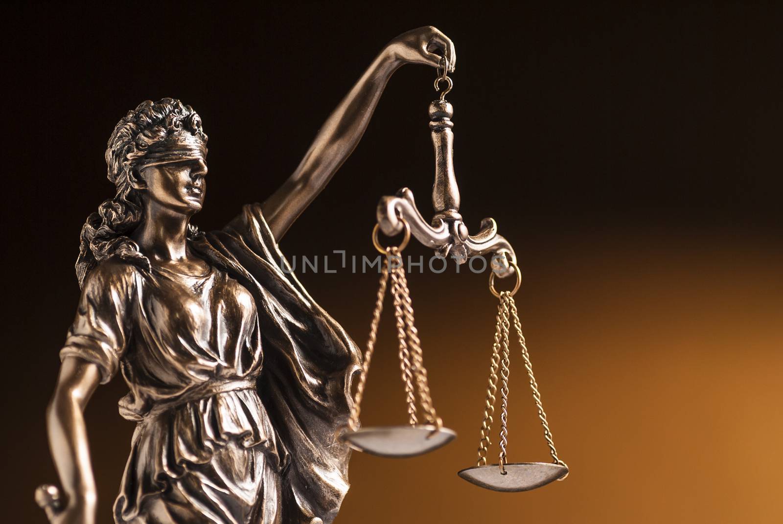 A blindfolded bronze statue of Justice holding up the scales or law and order in a close up partial view on a brown background with copy space