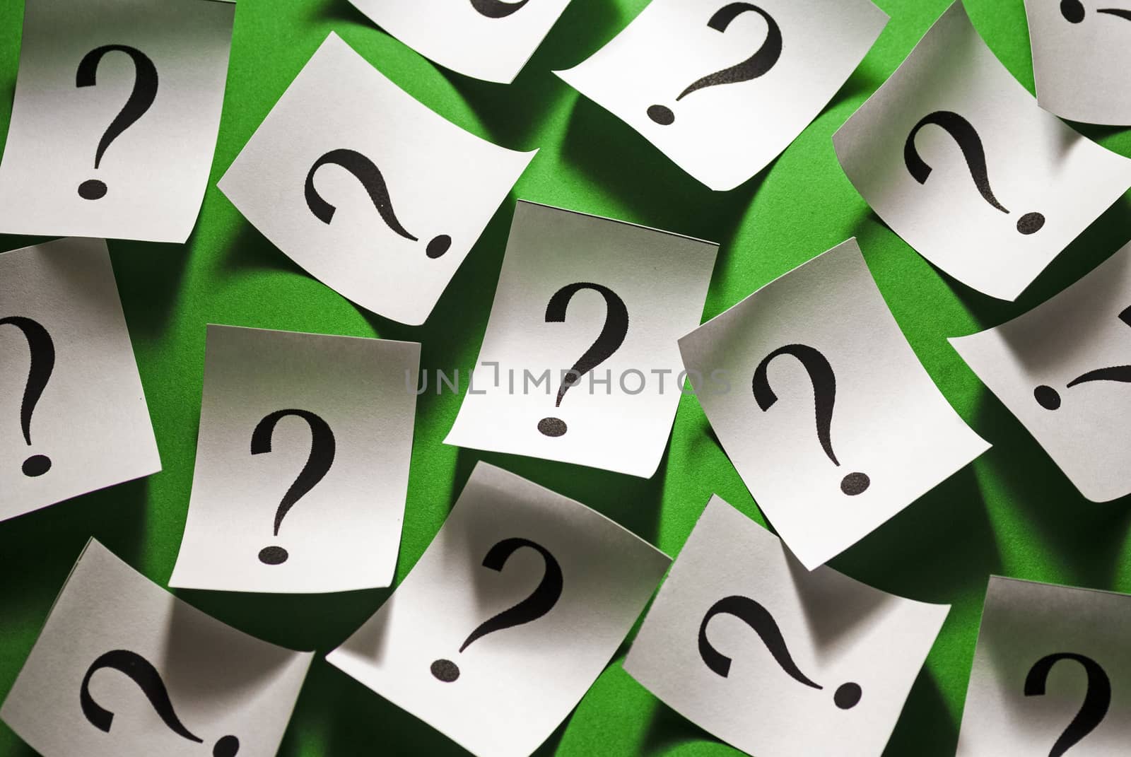 Randomly scattered question marks on white paper over a colorful green background in a conceptual image