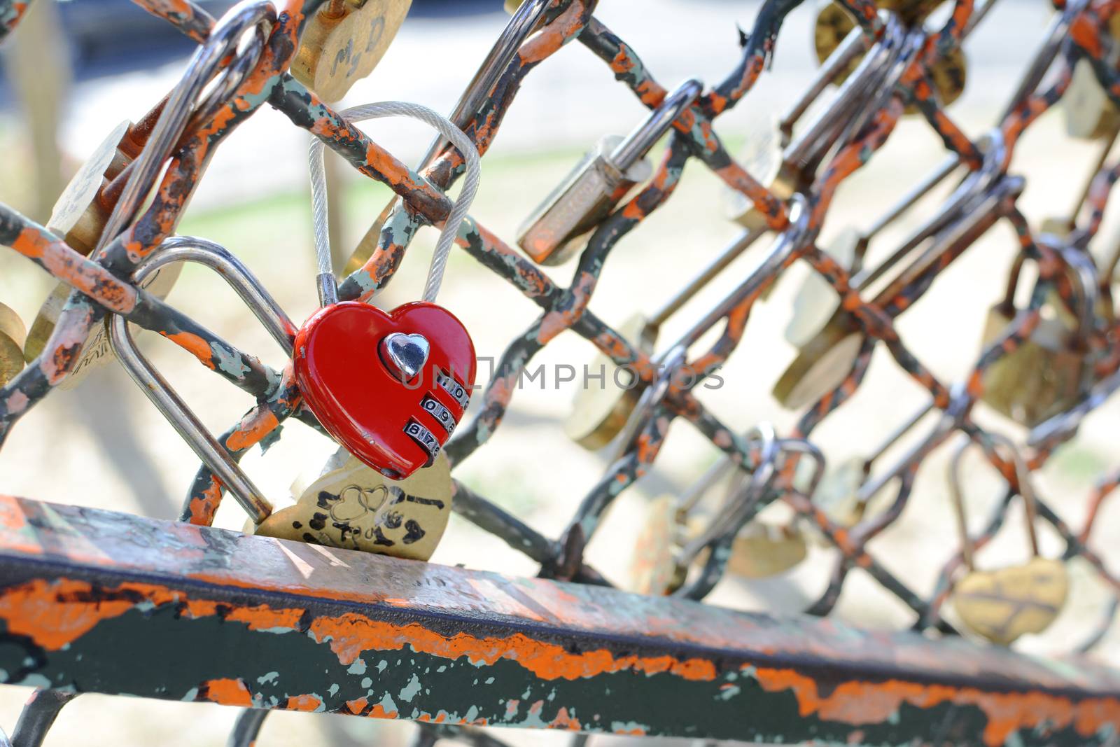 Red heart-shaped combination padlock fastened to metal fence  by sarahdoow