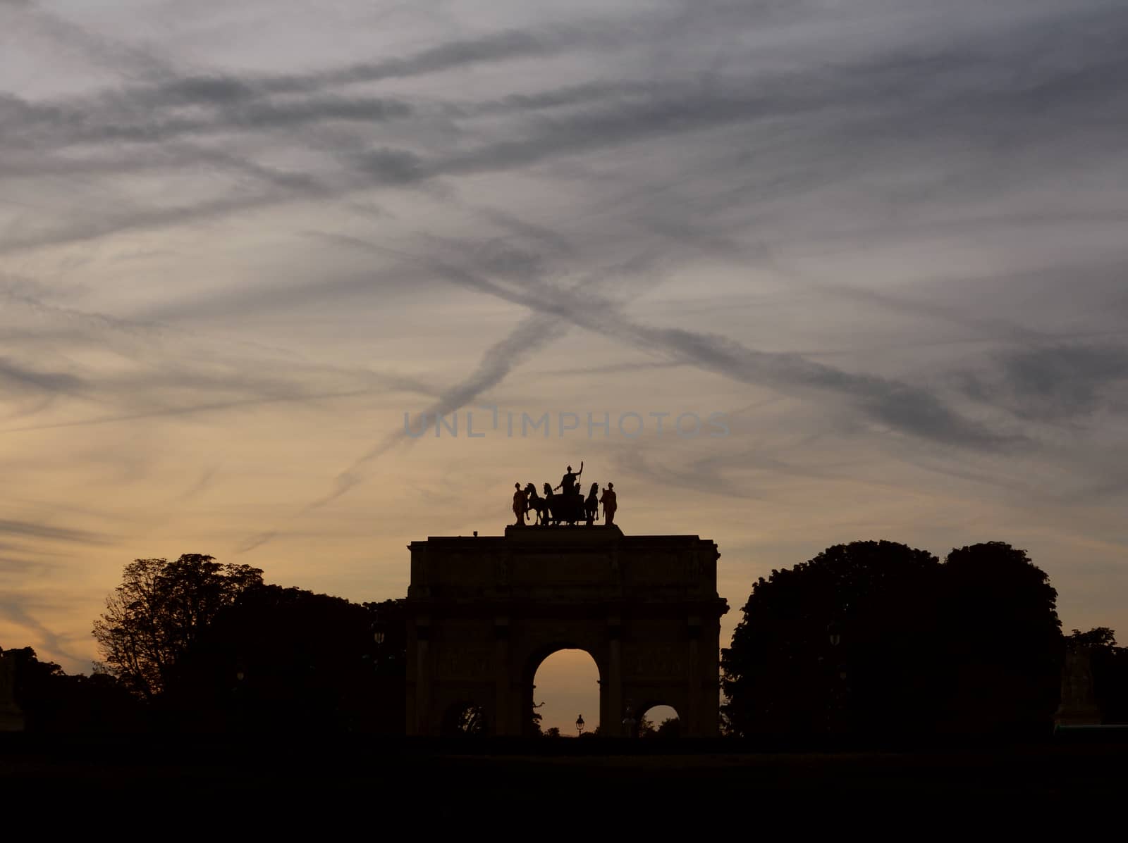 Arc de Triomphe du Carrousel near the Louvre in Paris in silhouette against a twilight sky covered in contrails