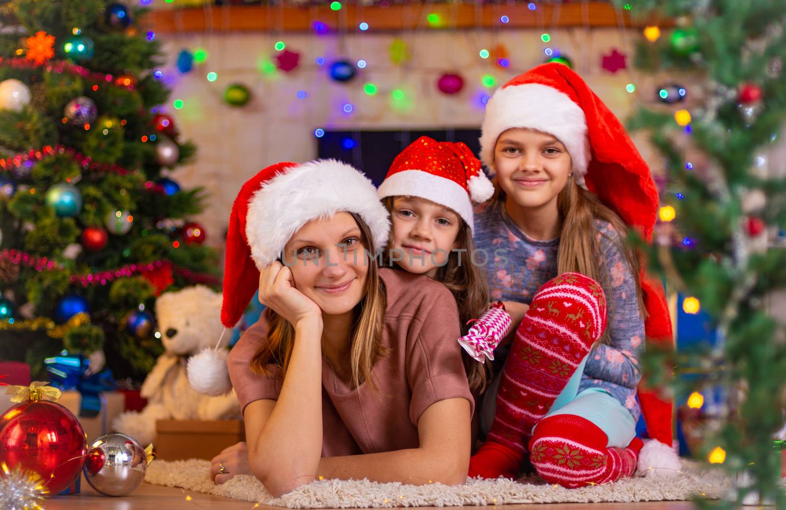 Mom and two daughters lie on the floor of a Christmas tree