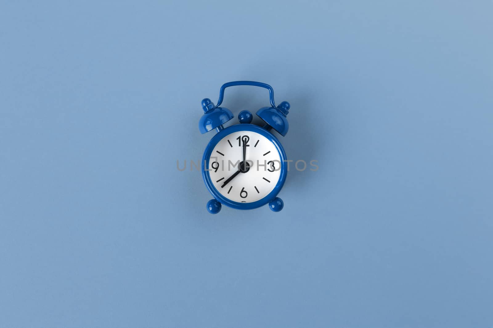 Small alarm clock on pastel background in Classic Blue colour, close-up, top view. Minimal retro style. Time management, Color of the year 2020 concept. Copy space for text. Horizontal orientation.