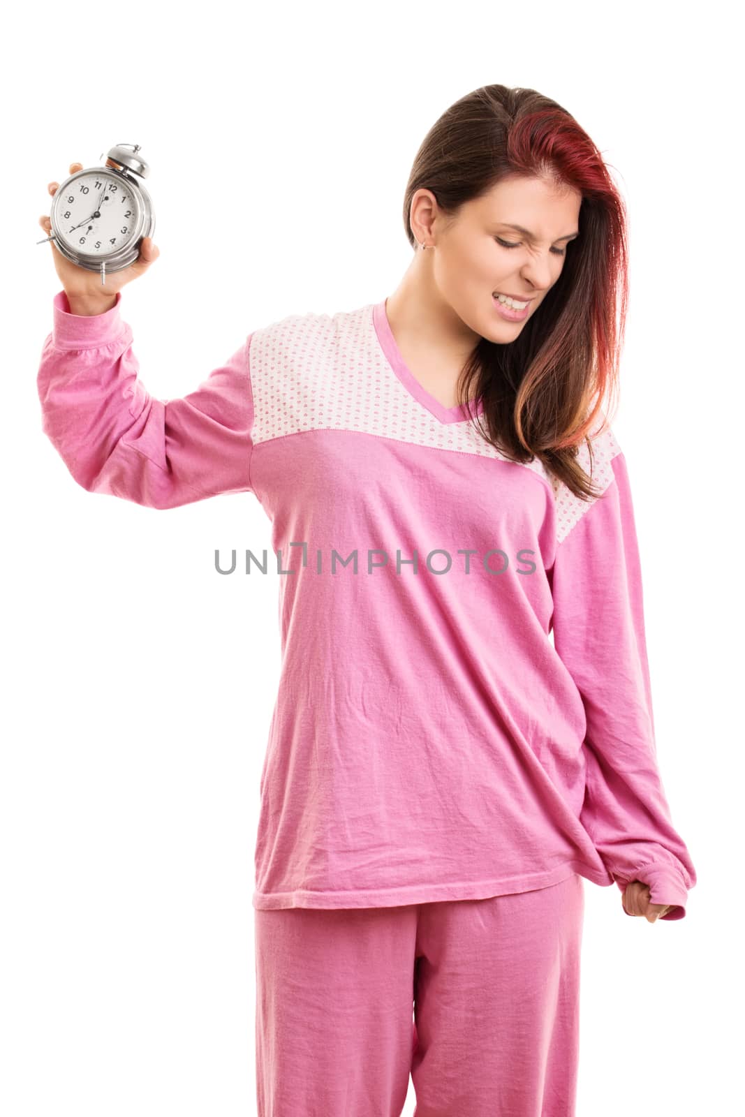 Early morning concept. Angry young woman in pink pajamas throwing a ringing alarm clock to the ground, isolated on white background. Annoyed young girl throwing alarm clock.