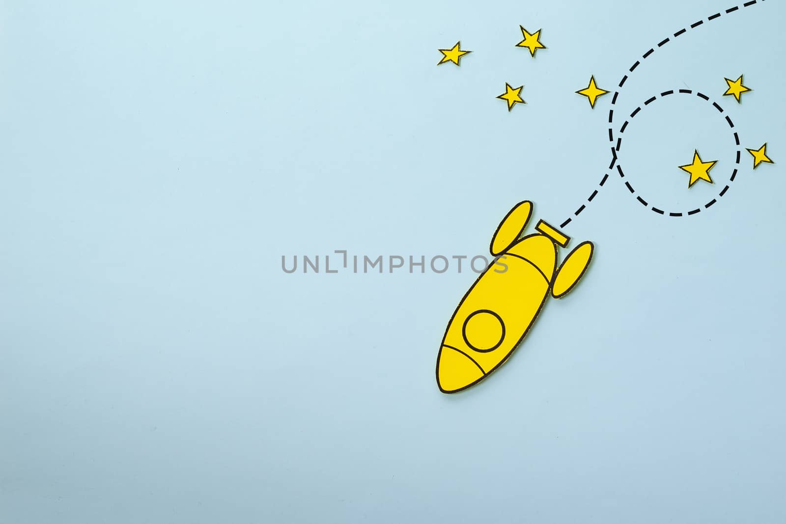 Little yellow rocket looping around stars on its way back to earth over a blue background with copy space