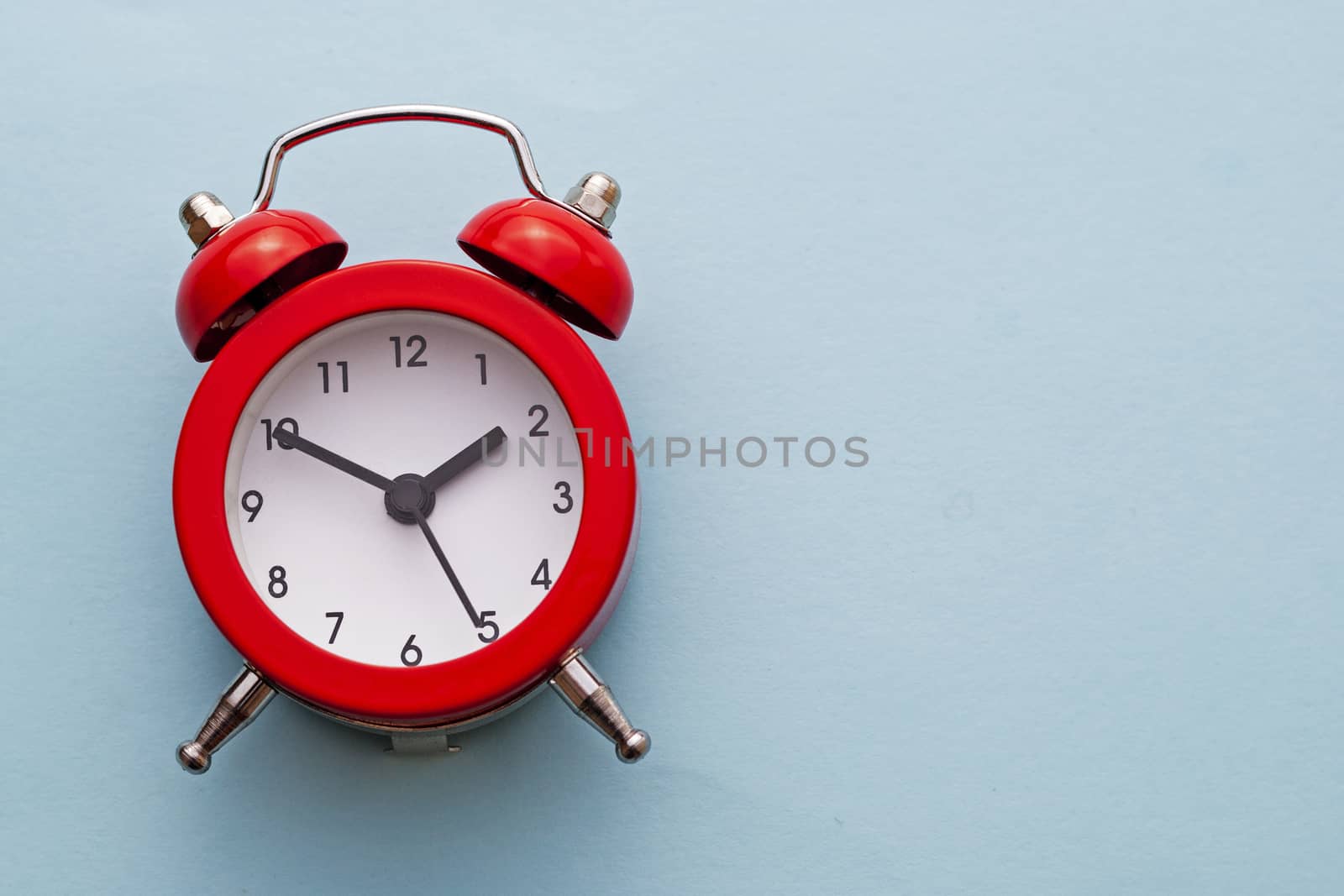 Colorful red traditional alarm clock with bells on a bright blue background with copy space placed to the side