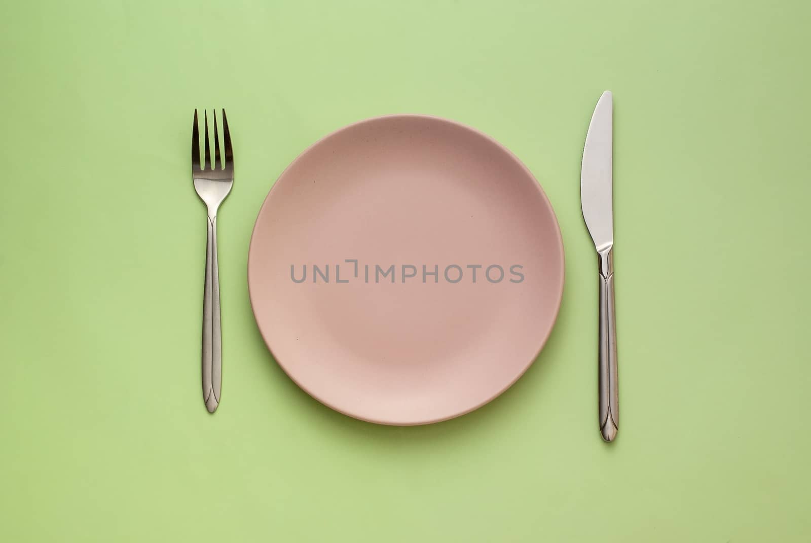 Empty pink plate with utensils on a green background viewed from overhead in a dining and food concept