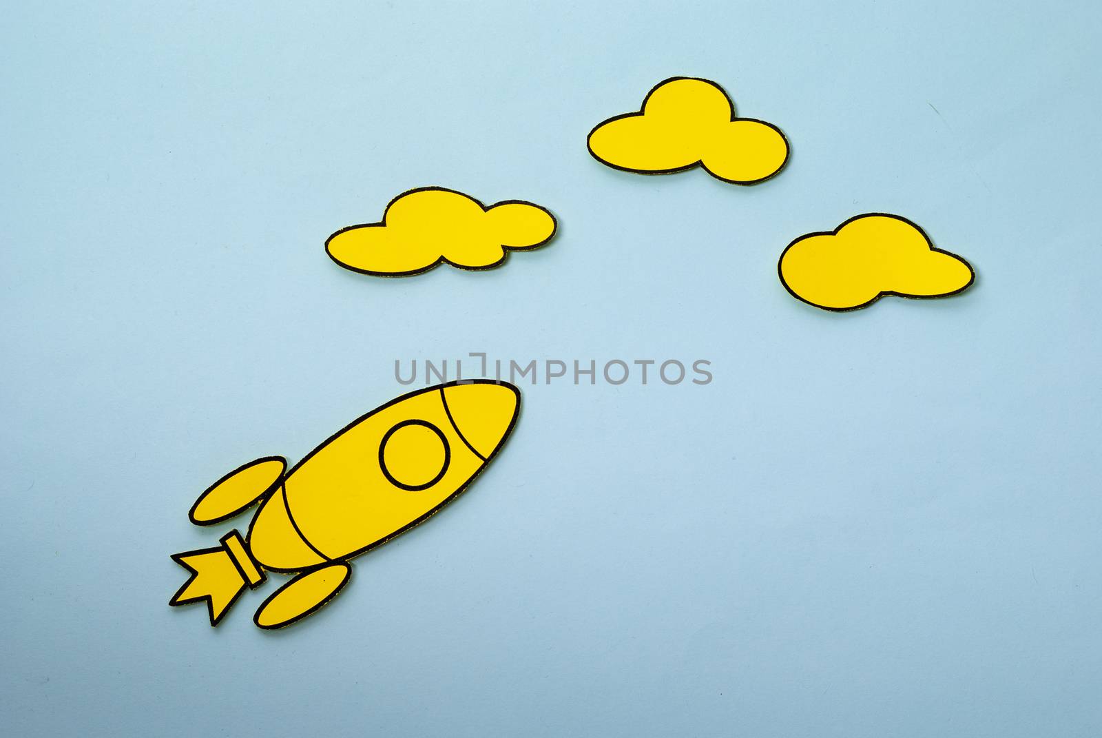 Little yellow rocket flying high aiming for the clouds in a concept of ambition and success over a blue background with copy space