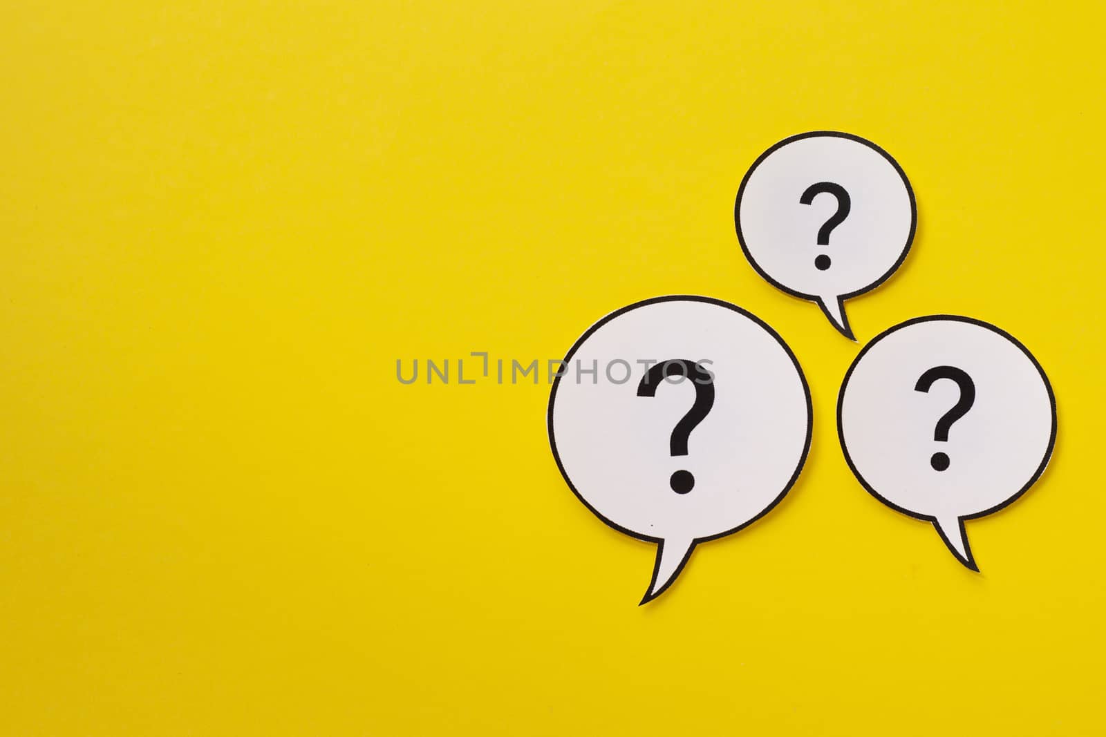 Three speech bubbles with question marks over a bright yellow background with copy space