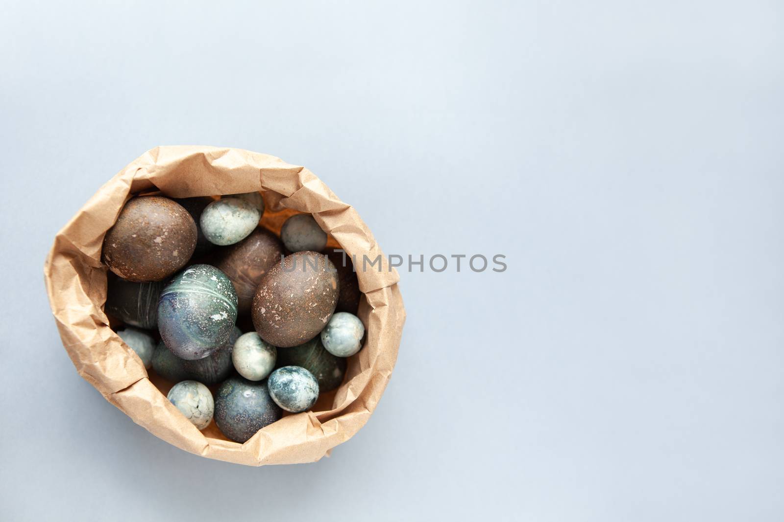 Creatively painted chicken and quail Easter eggs with natural hibiscus dye, look like sea stones in craft bag on a gray background. Happy Easter DIY concept. Soft slective focus. Flat lay, copy space.
