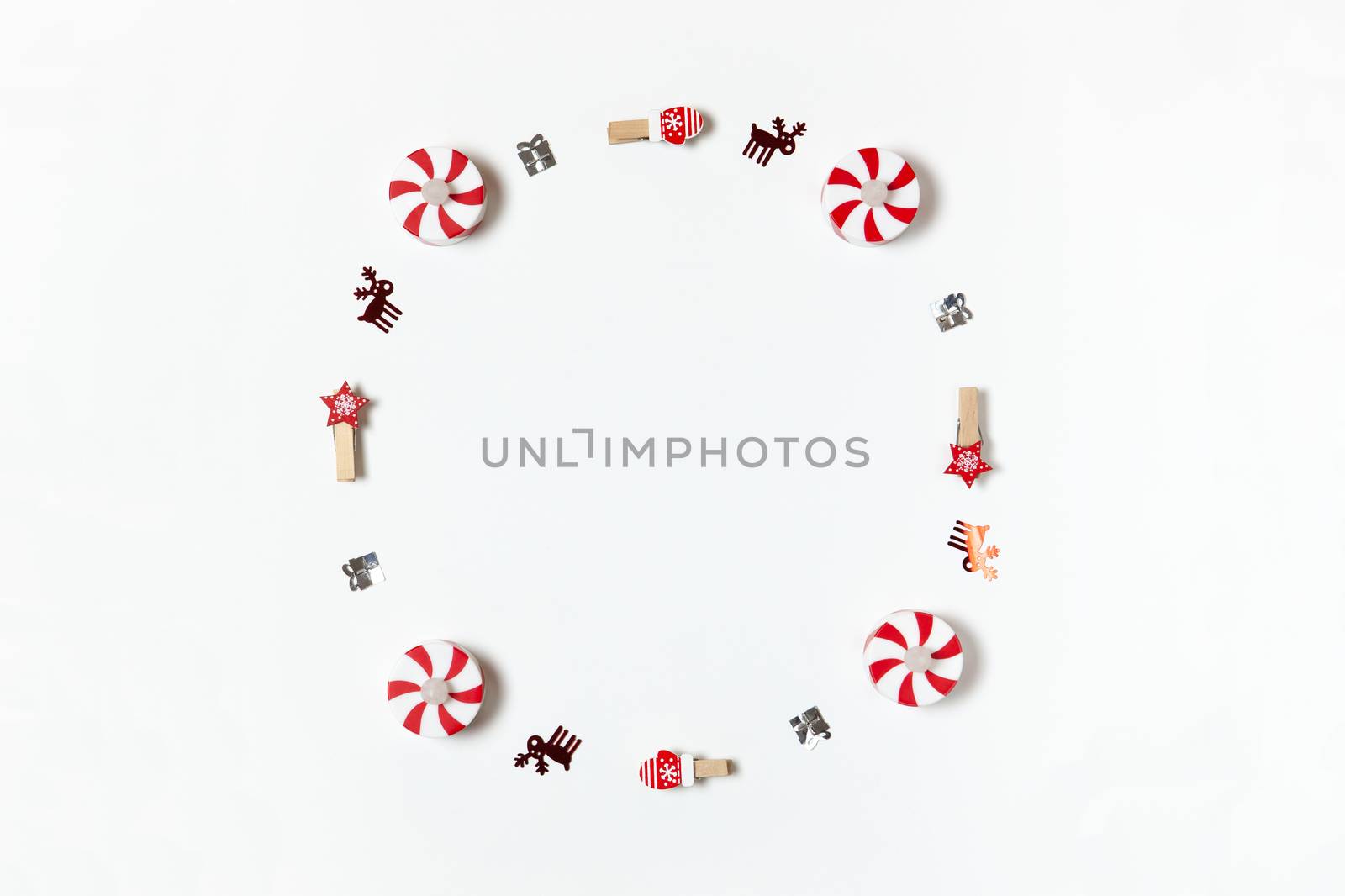 Simple Christmas composition. Round frame of clothespins, candy-bulbs, deer confetti and gifts on white background, copy space. Horizontal. Minimal style. Top view. For social media, greeting card.