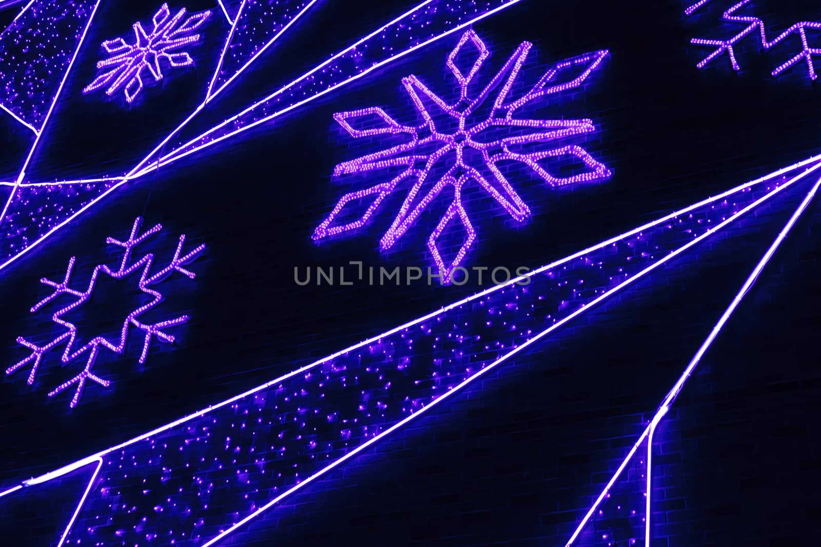 Neon blue lights in the shape of snowflakes on a brick wall. Festive illumination of the night city.