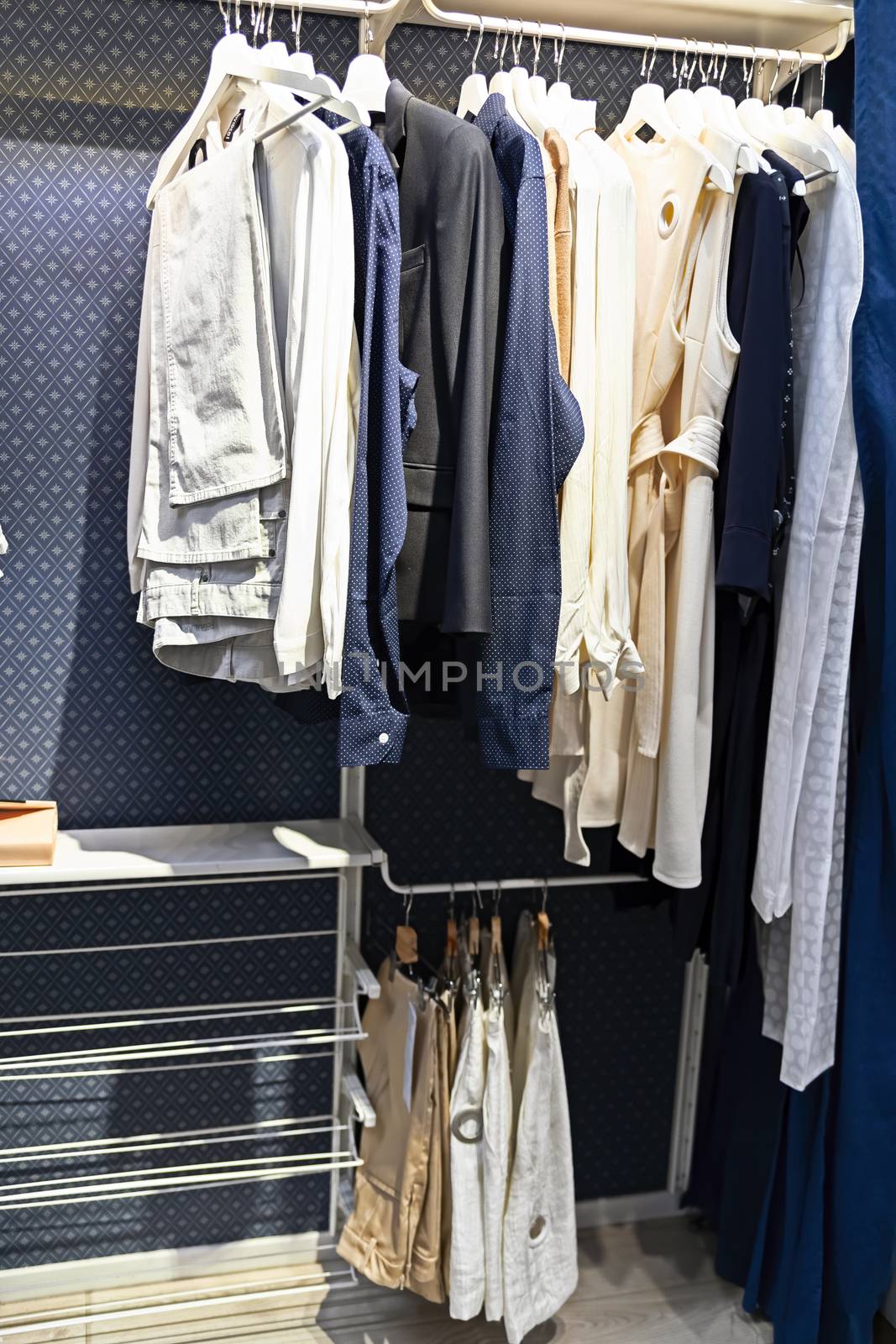A number of different clothes hang on hangers in a modern blue closet. by bonilook