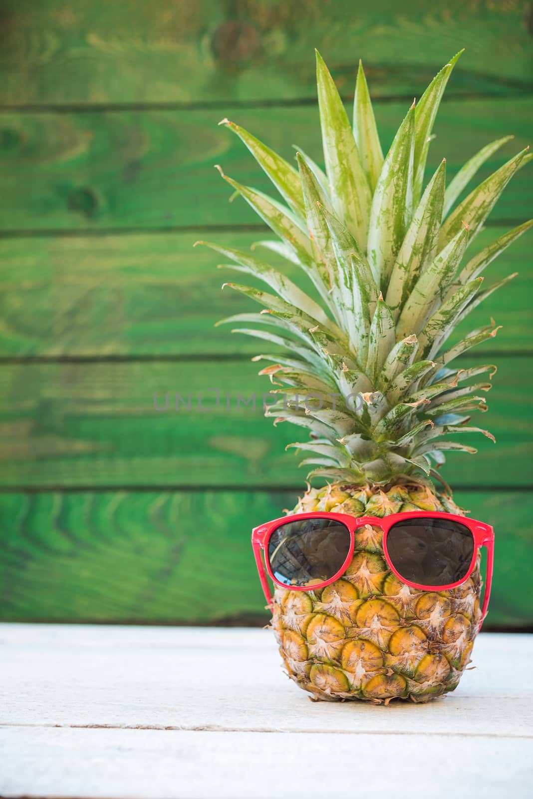 Holiday pineapple have sunglasses on green wooden background by Sorapop