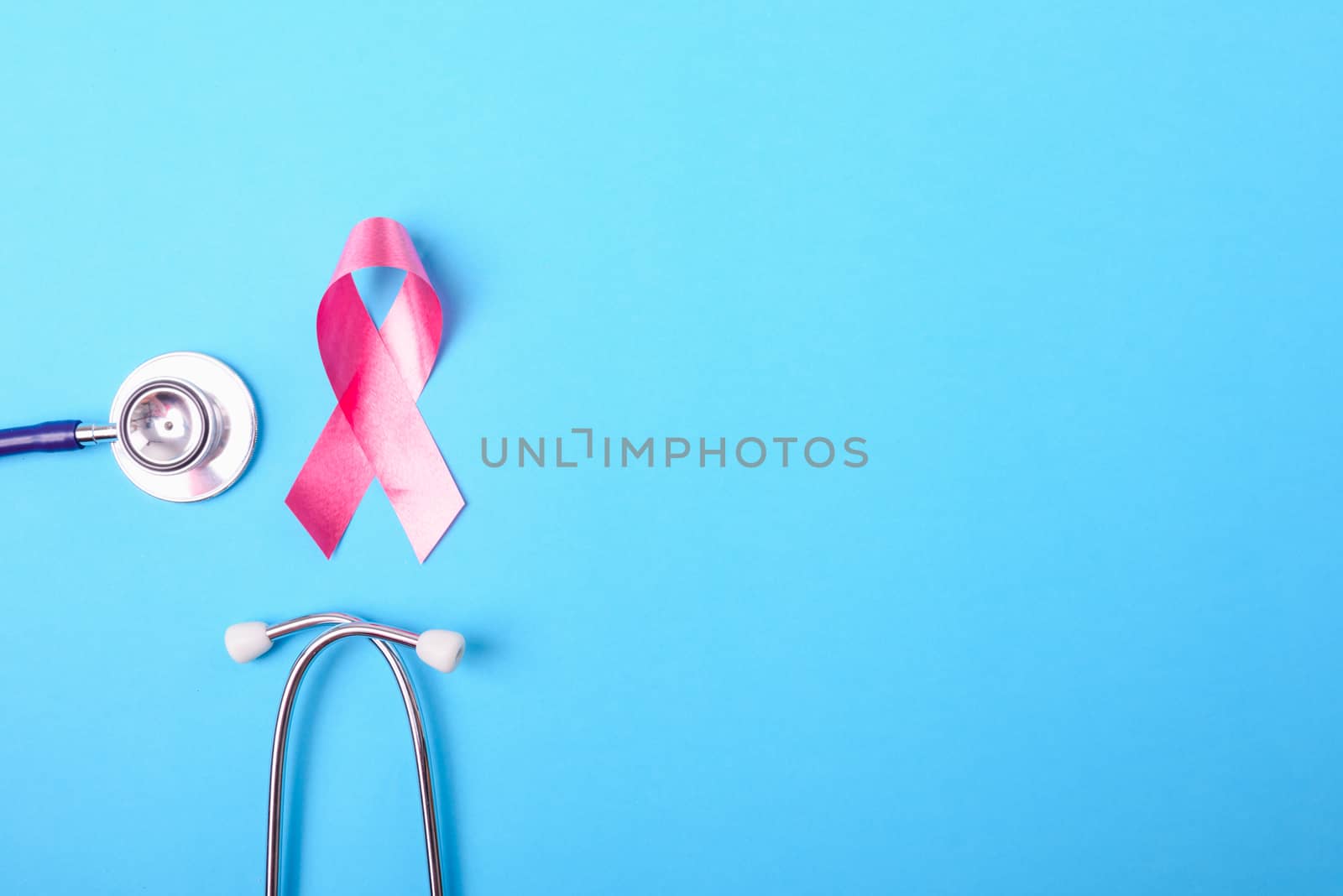 Breast cancer month concept, flat lay top view, pink ribbon and stethoscope on blue background with copy space for your text