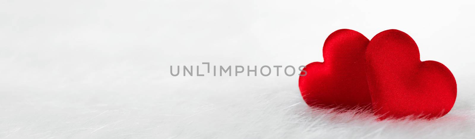 Two red silk hearts on white fur background with copy space for text