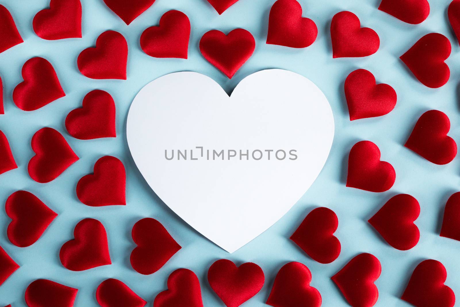 Valentine's day many red silk hearts and white heart shaped card on blue background, love concept