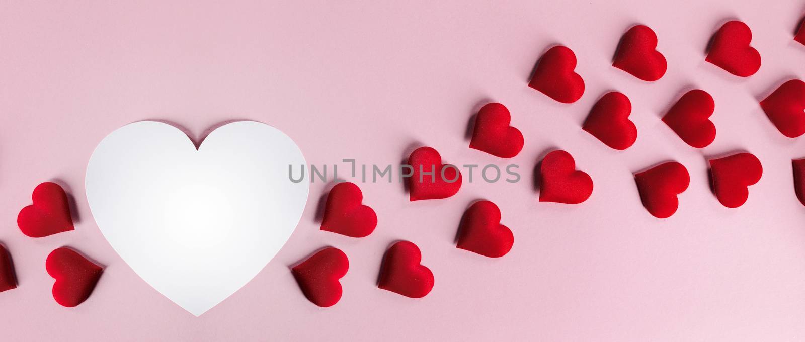 Valentine's day many red silk hearts and white heart shape card on pink paper background , border frame on red with copy space, love concept