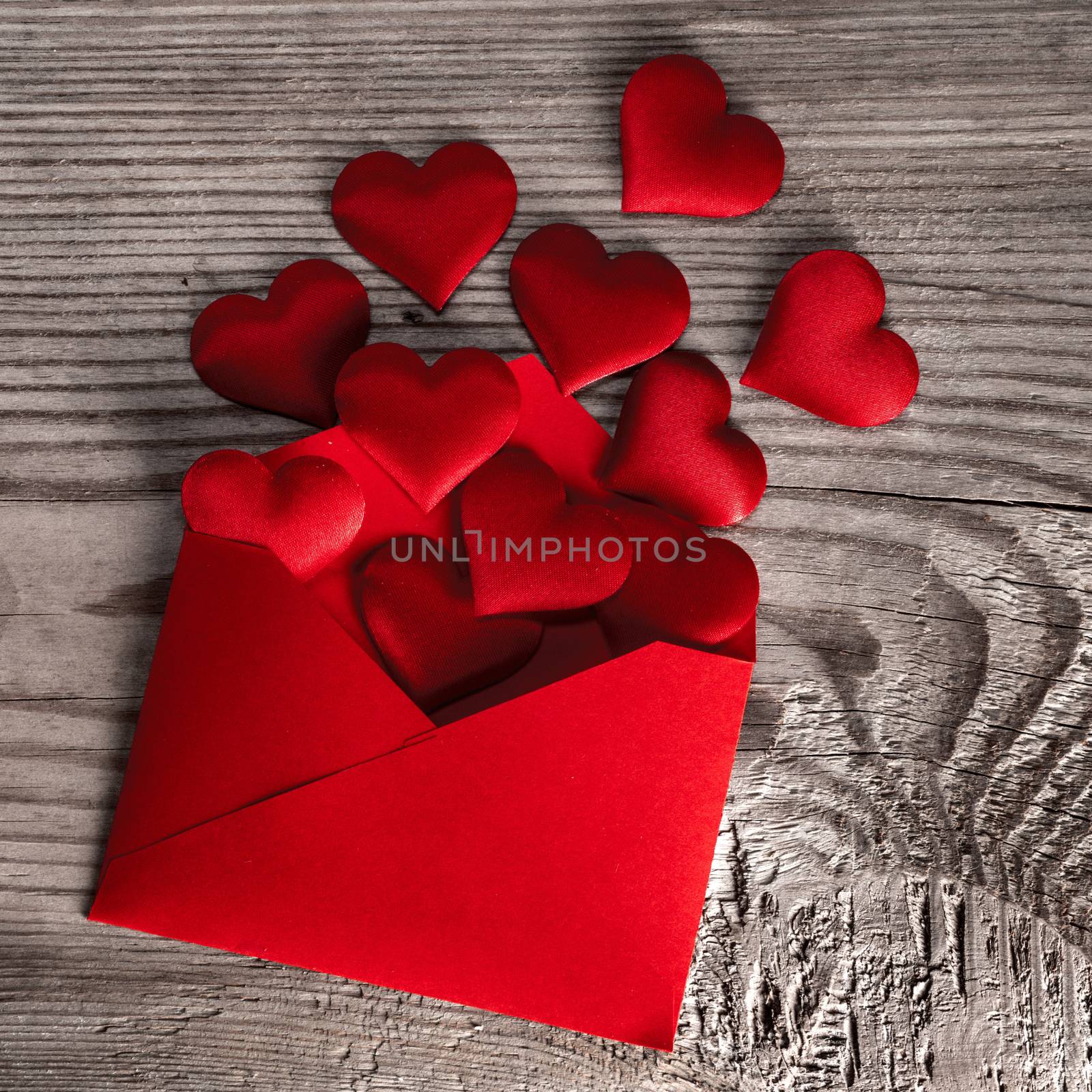 Valentine day love letter, envelope of craft red paper with red hearts heap spread on wood background.