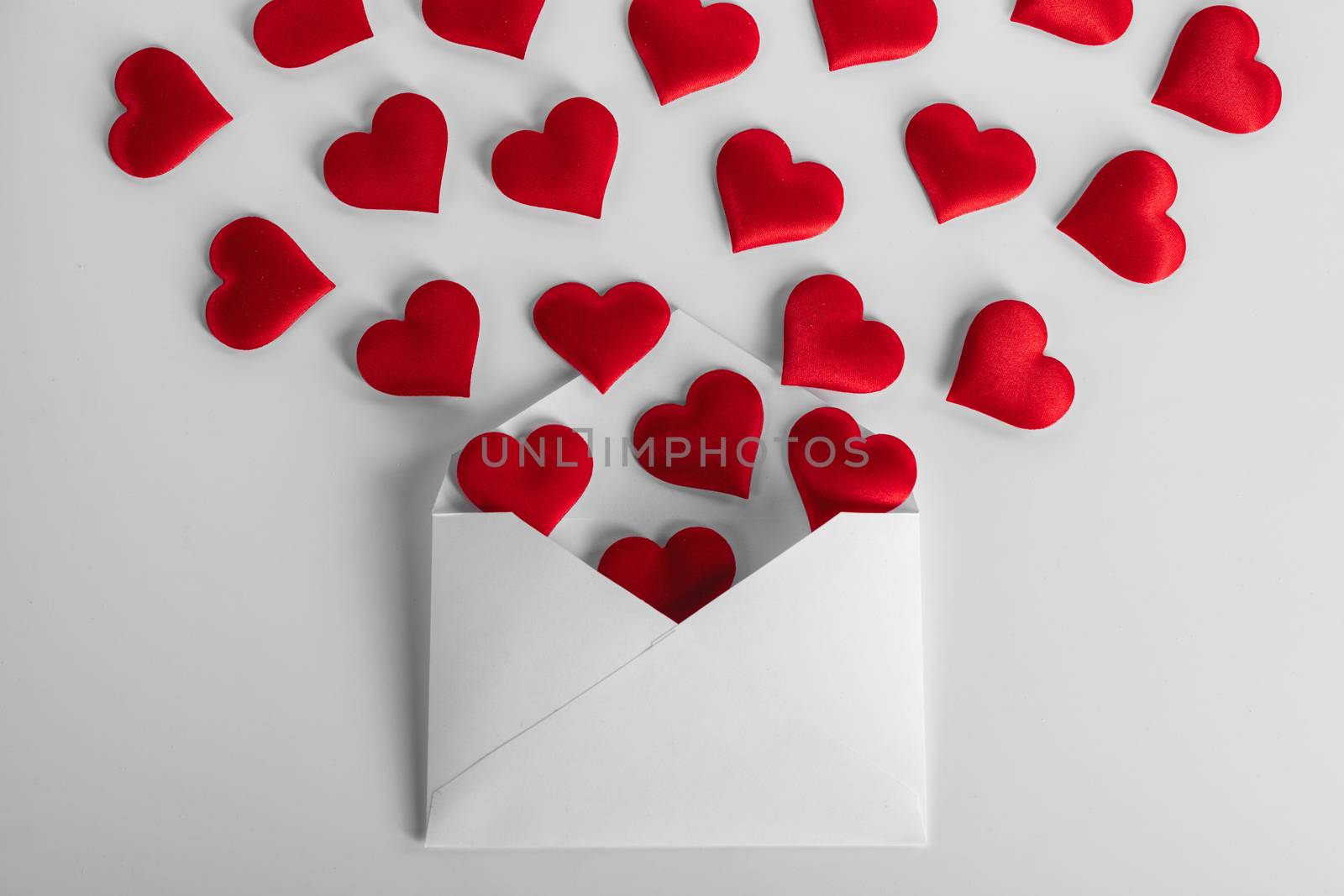 Valentine day love letter, envelope of craft paper with red hearts heap spread on white background.