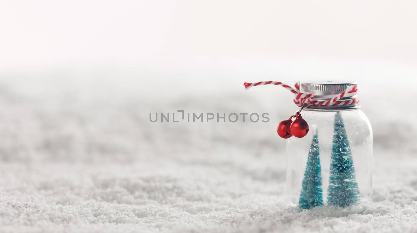 Christmas ornaments of glass jar with striped ribbon , bells and fir trees inside on snow background