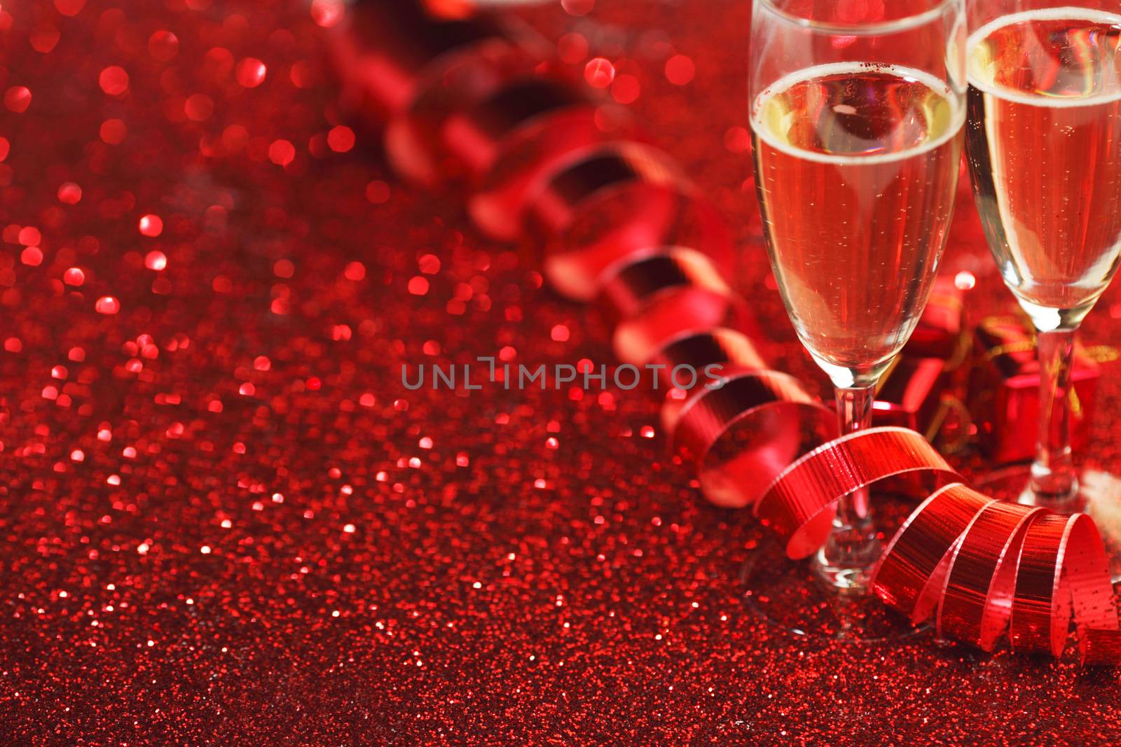Glasses with Champagne and gifts on red glitters background