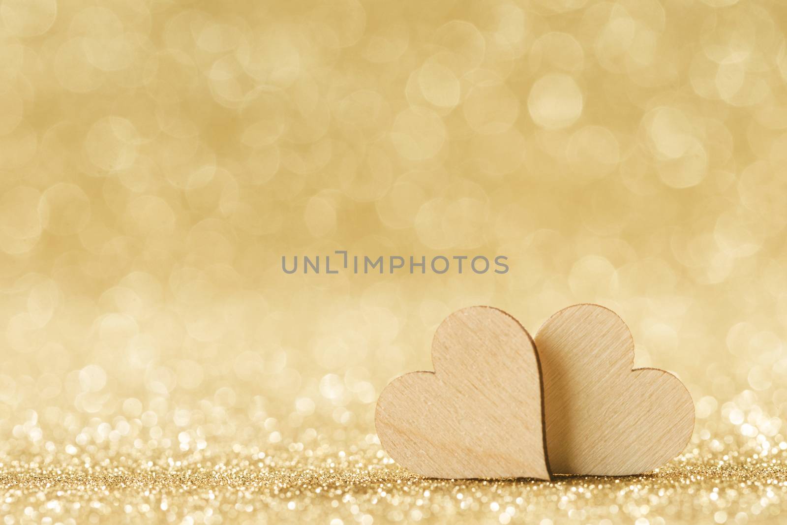 Two small handmade wooden hearts on bright golden lights bokeh background Valentines day card