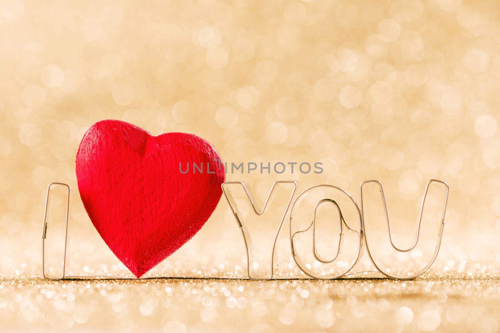 Red handmade wooden heart and words I love you on golden bright glitter lights bokeh background