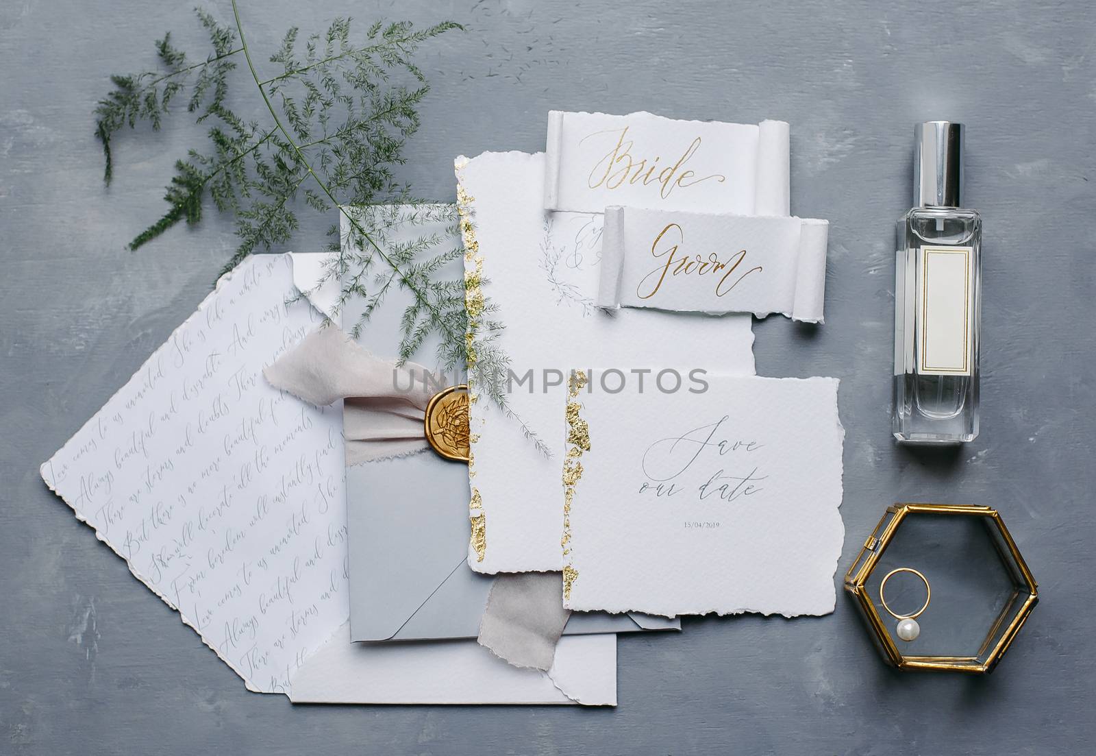 Wedding details flat lay. Wedding invitation and scroll paper. Bottle with fragrance. Simple bouquet. Ring box.