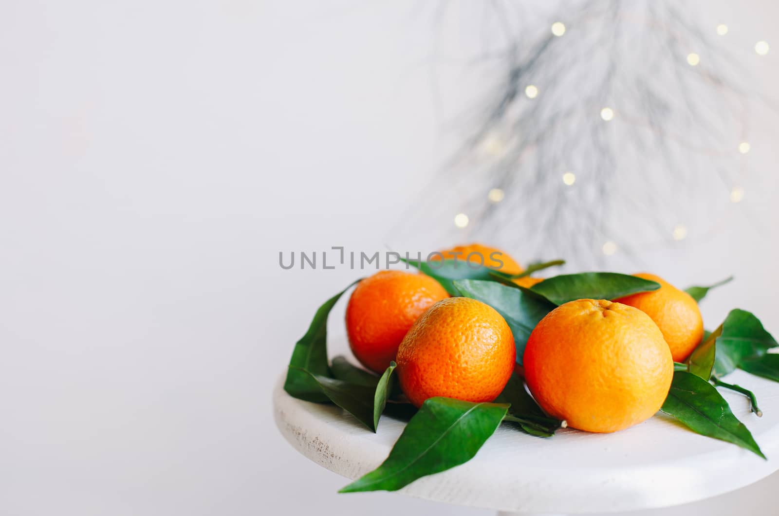 Orange tangerines on grey background in New Year's decor with brown pine cones and green leaves. Delicious sweet clementine. Christmas decoration with mandarins.