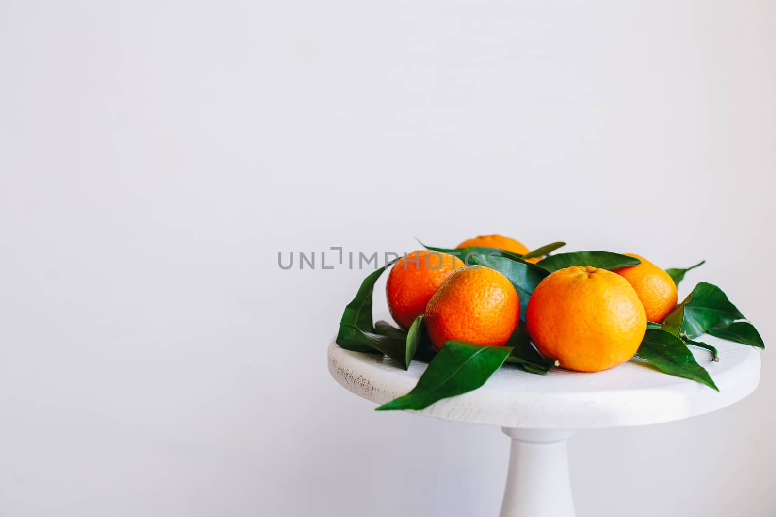 Orange tangerines on grey background in New Year's decor with brown pine cones and green leaves. Delicious sweet clementine. Christmas decoration with mandarins.