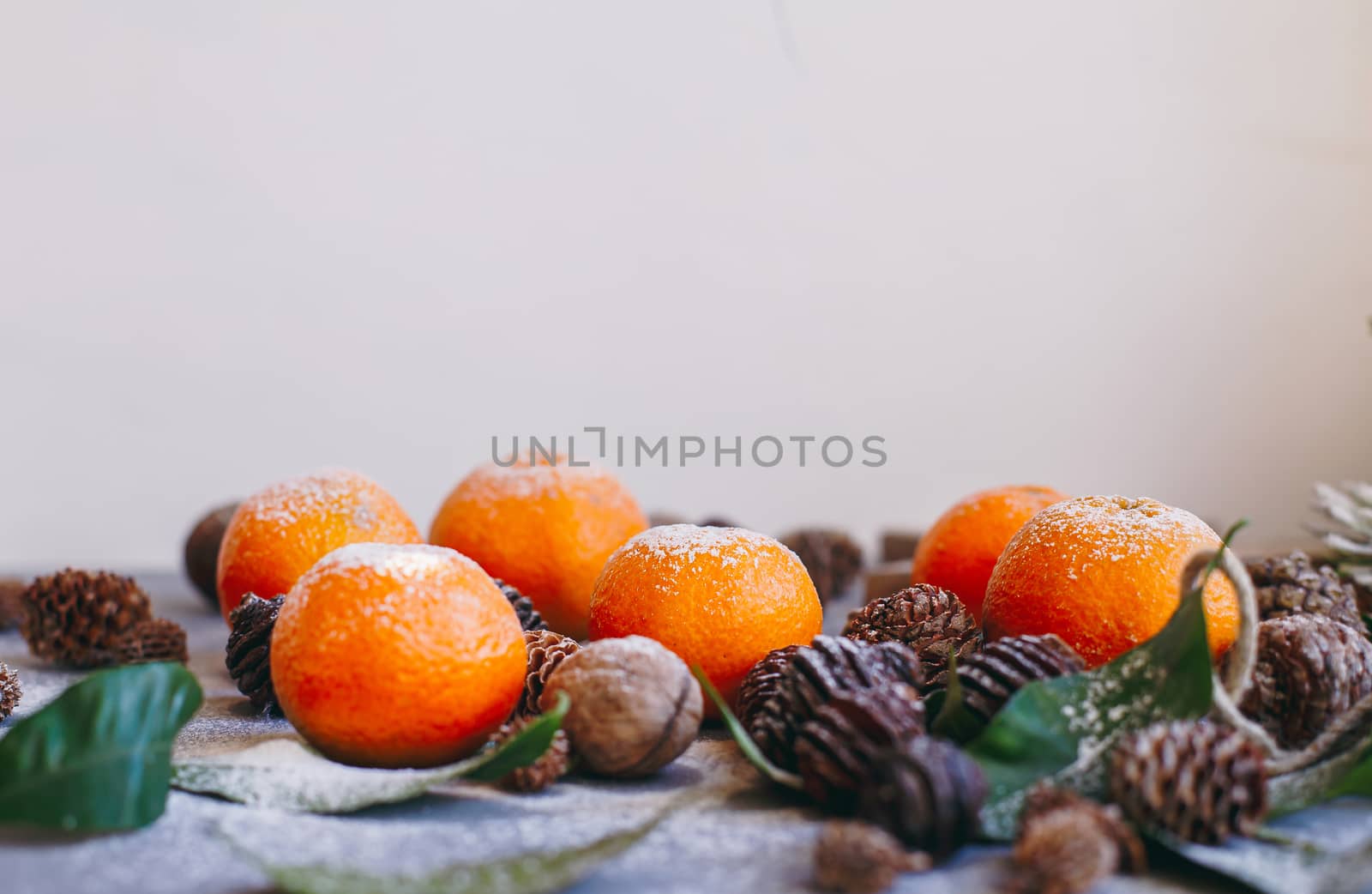 Orange tangerines on grey background in New Year's decor with brown pine cones and green leaves. Delicious sweet clementine. Christmas decoration with mandarins.