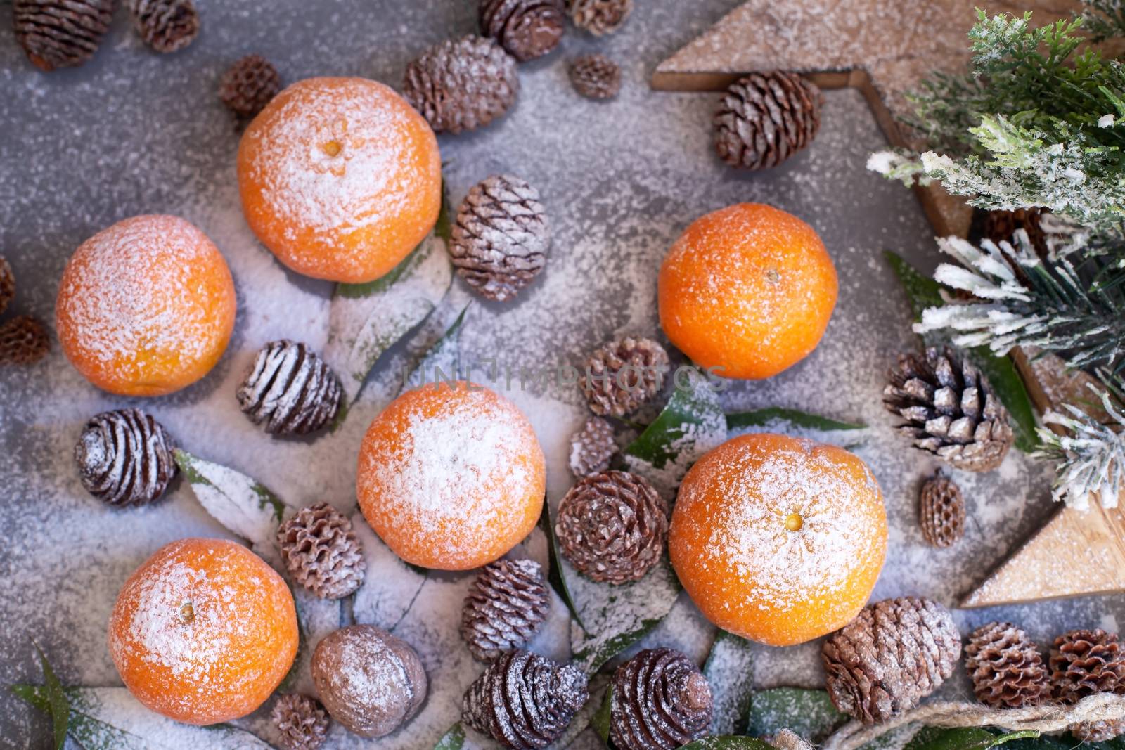 Orange tangerines on grey background in New Year's decor with brown pine cones and green leaves. Delicious sweet clementine. Christmas decoration with mandarins.