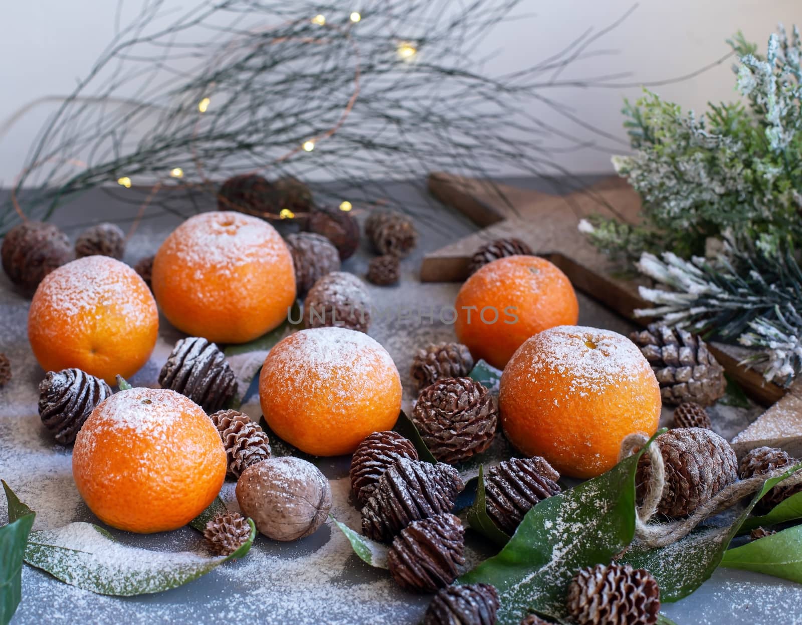 Orange tangerines on grey background in New Year's decor with brown pine cones and green leaves. Delicious sweet clementine. Christmas decoration with mandarins.