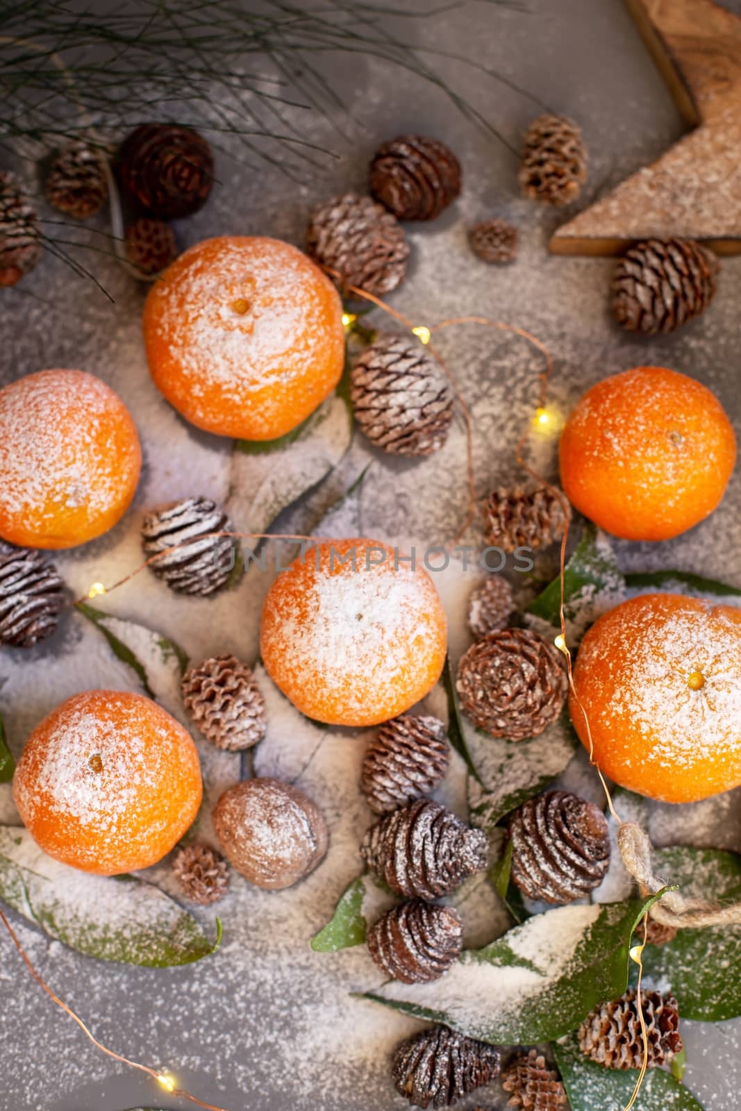 Orange tangerines on grey background in New Year's decor with brown pine cones and green leaves. Delicious sweet clementine. Christmas decoration with mandarins.