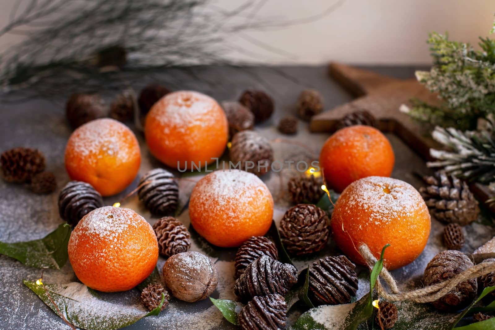 Orange tangerines on grey background in New Year's decor with brown pine cones and green leaves. Delicious sweet clementine. Christmas decoration with mandarins.