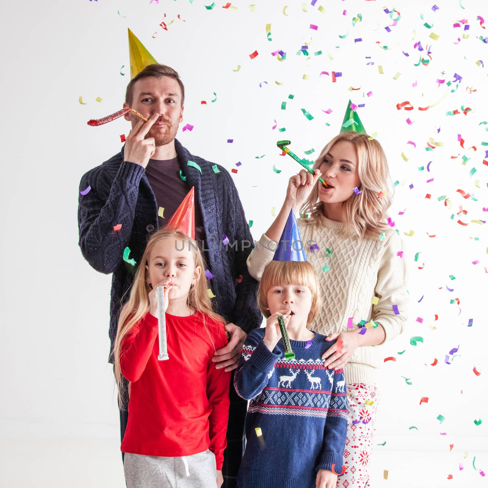 Family blowing party trumpets with confetti celebrating new year, gray background with copy space for text