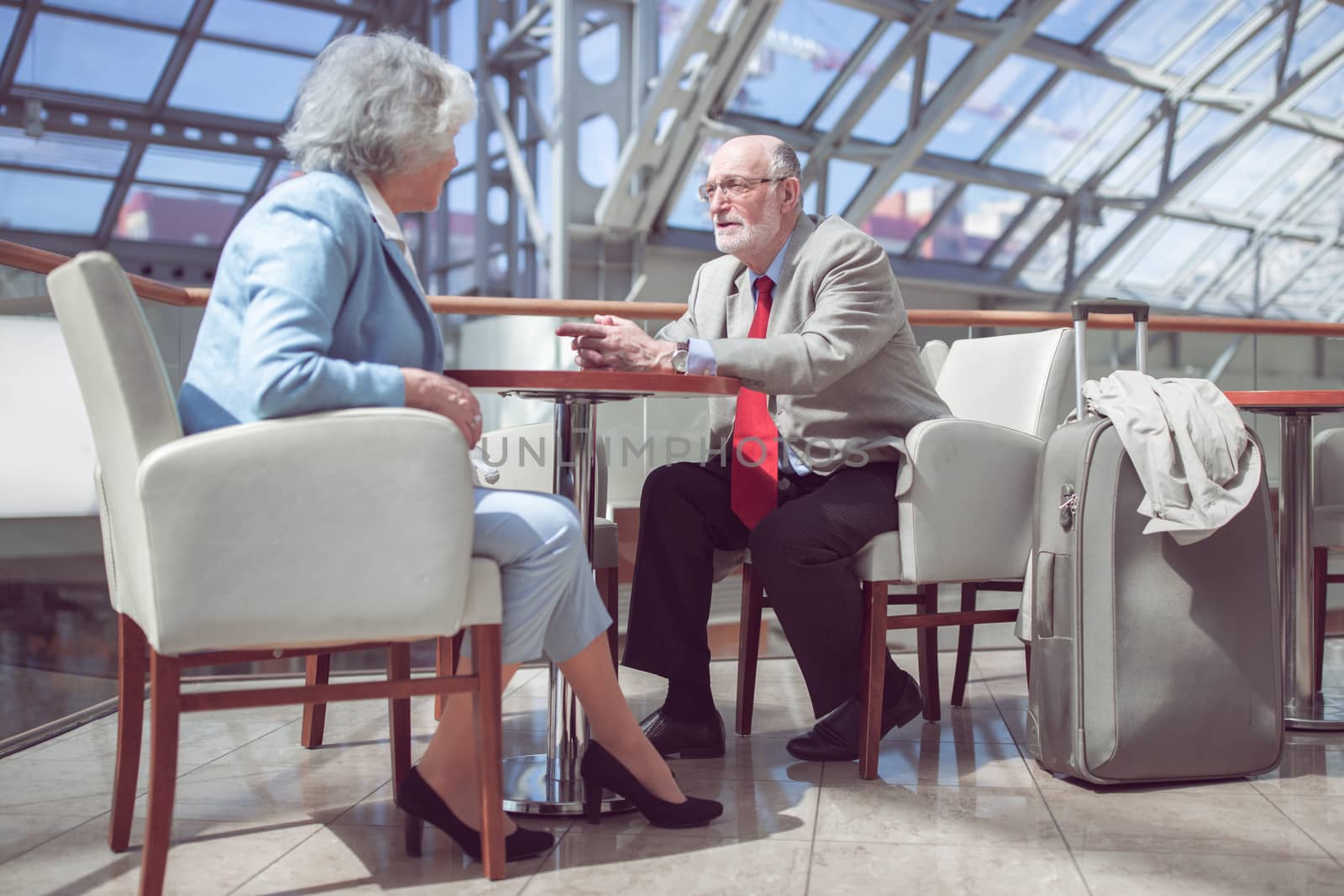 Happy elderly senior couple of travelers with suitcase in airport cafe waiting for flight