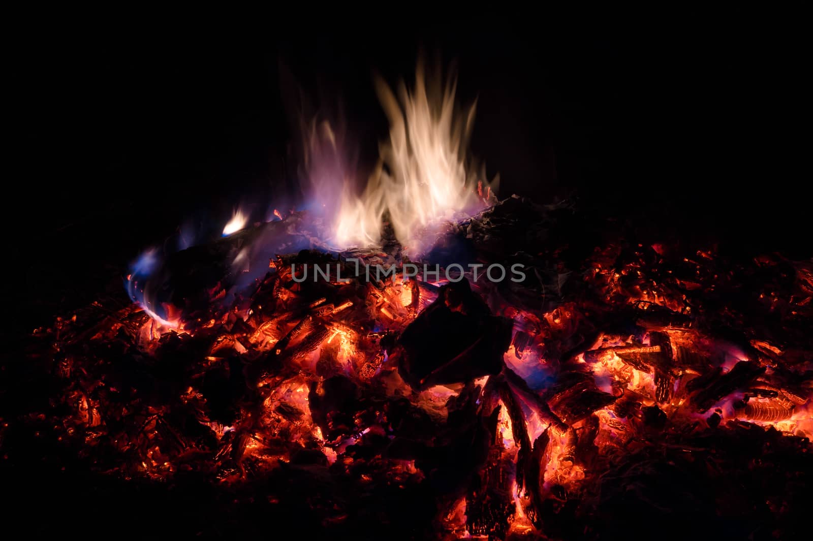 A low light long exposure photo of smouldering coals. Many coals and flames. Burning books and wood. 