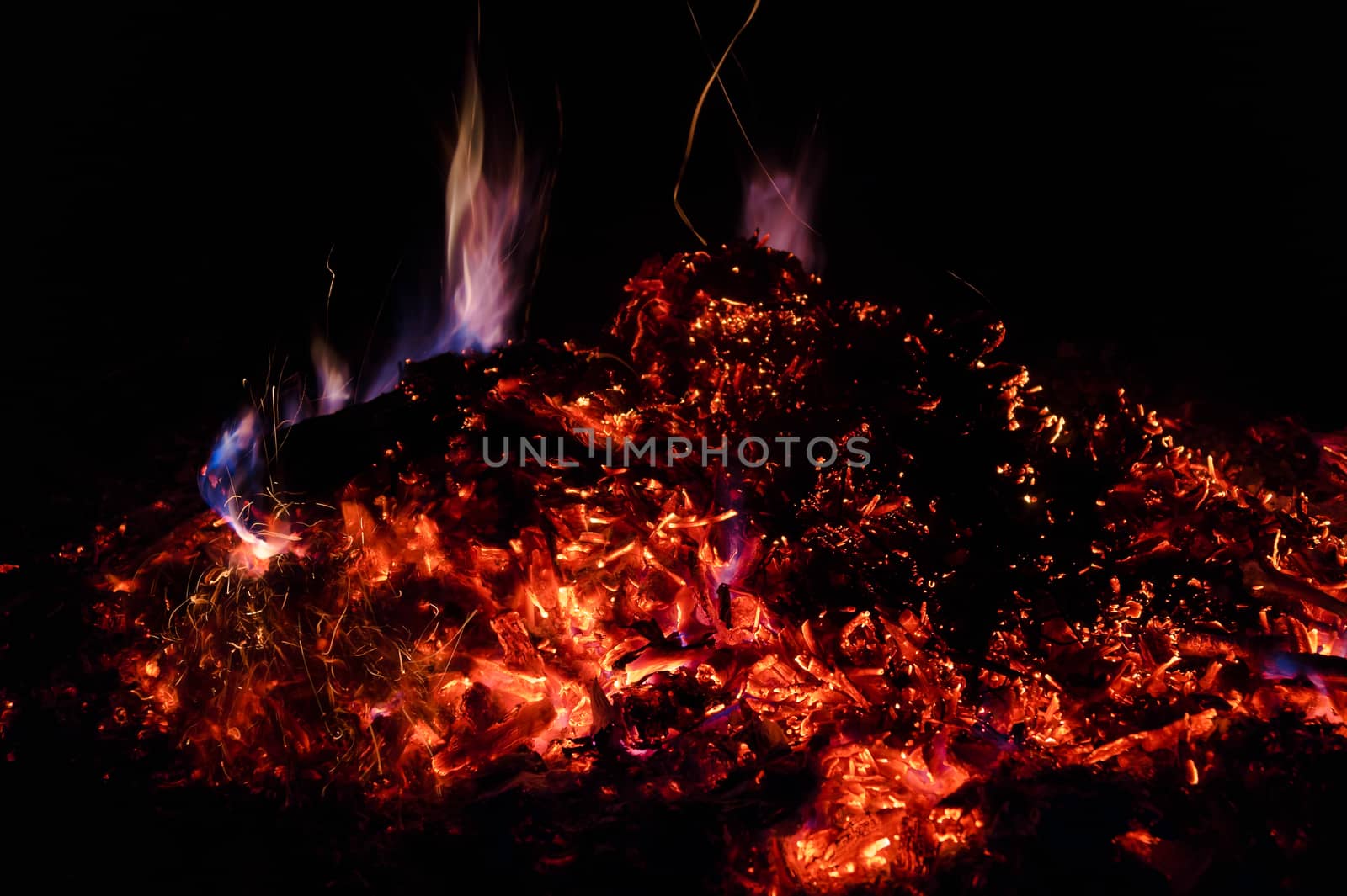 A low light long exposure photo of smouldering coals. Many coals and flames. Burning books and wood. 