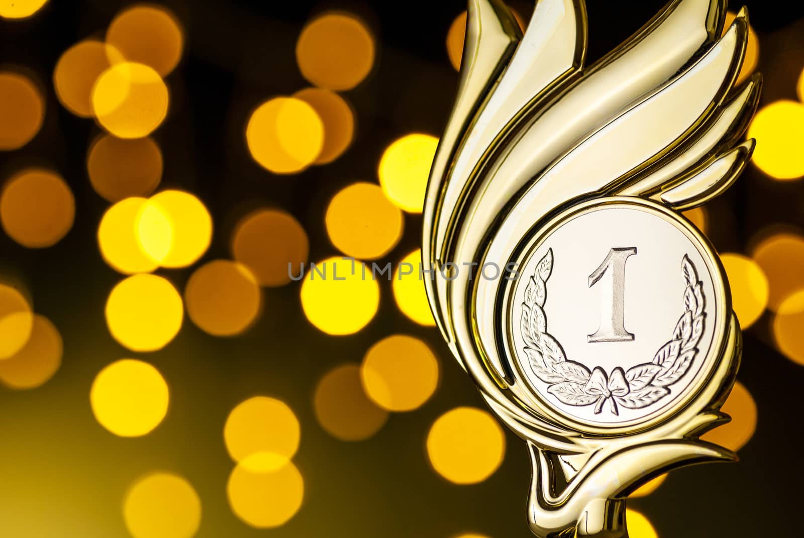 Gold award trophy for the winner of a competition or championship event with flaming medallion over a yellow party bokeh effect of golden light