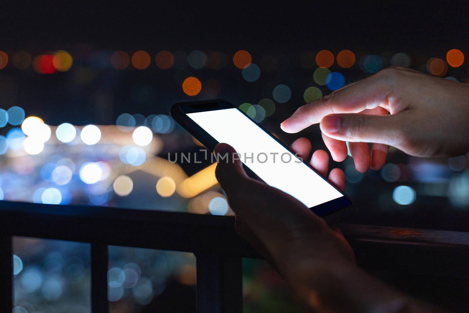 Shot of hands with smartphone in the city at night.