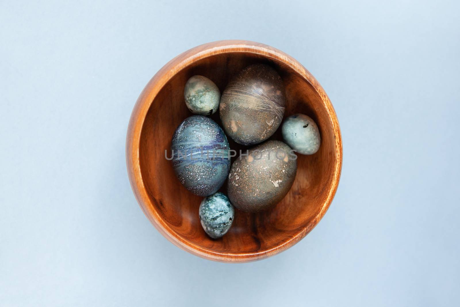 Creatively painted chicken and quail Easter eggs with natural hibiscus dye, look like sea stones in bowl on a gray background. Happy Easter DIY concept. Soft slective focus. Flat lay.