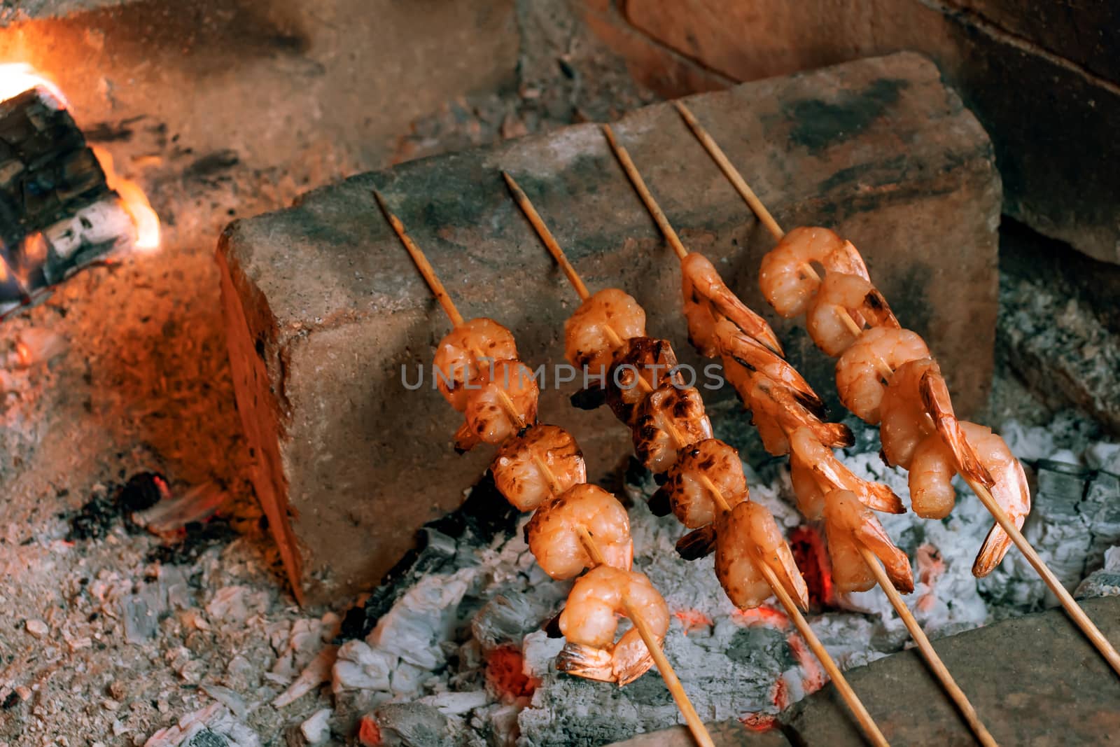 Shrimp frying on bamboo skewers on hot coals in a fireplace by galsand