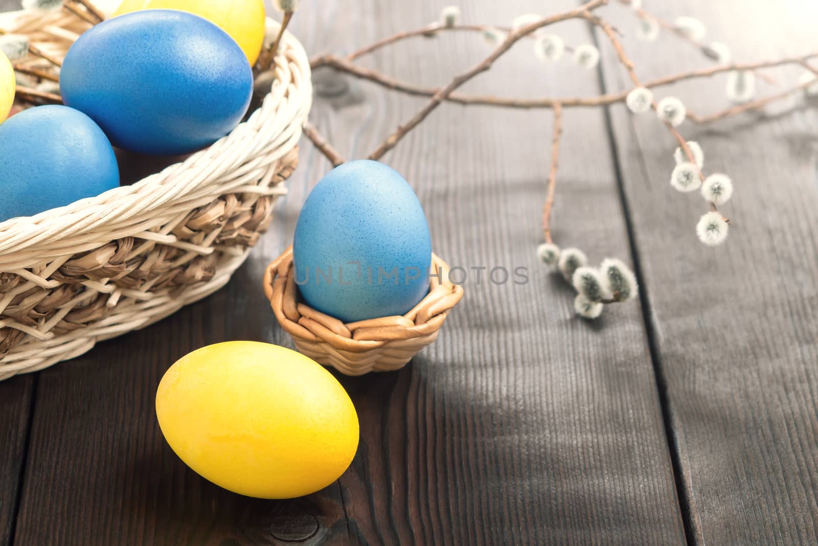 Easter composition - several colored eggs in a basket and on a dark wooden table with willow twigs.