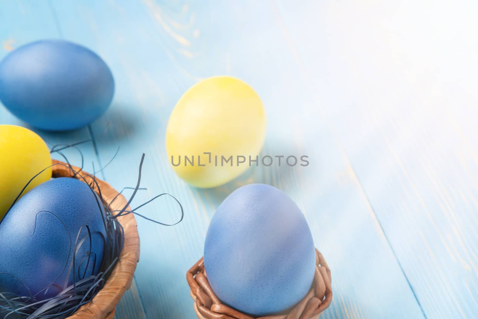 Easter composition - several colored eggs in a basket on a blue wooden table, place for text, copy space by galsand