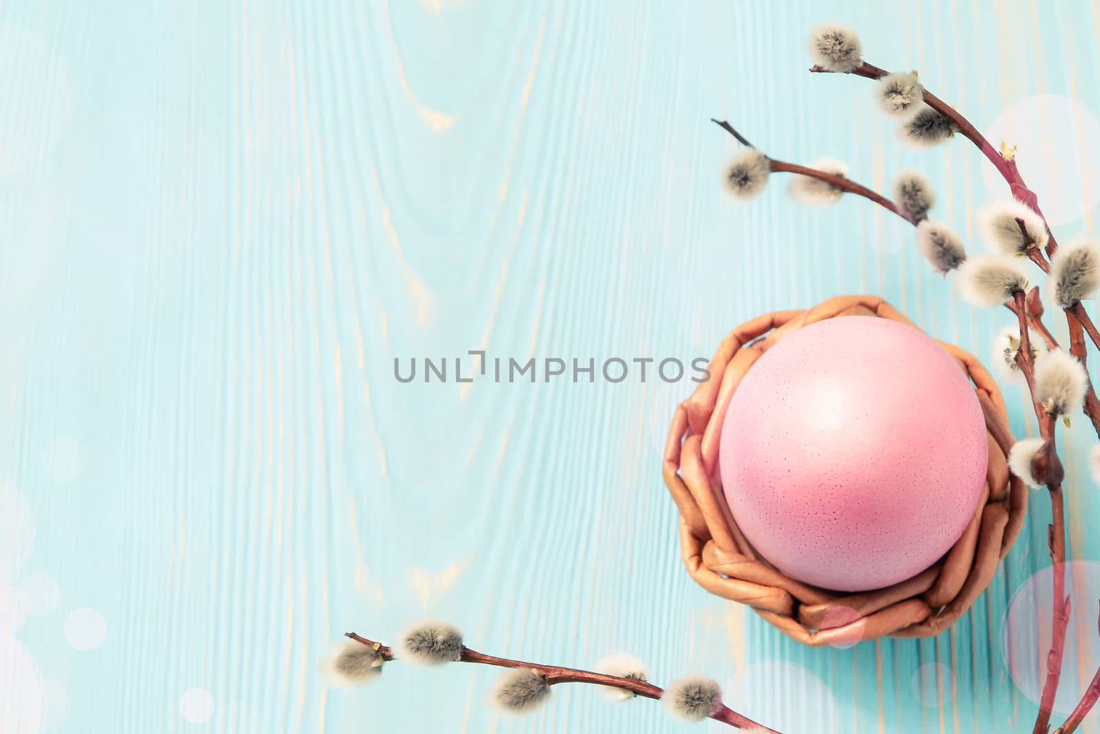 One pink egg in a wicker stand on a blue wooden table with pussy-willow twigs - blank for design or greeting card, place for text, copy space by galsand