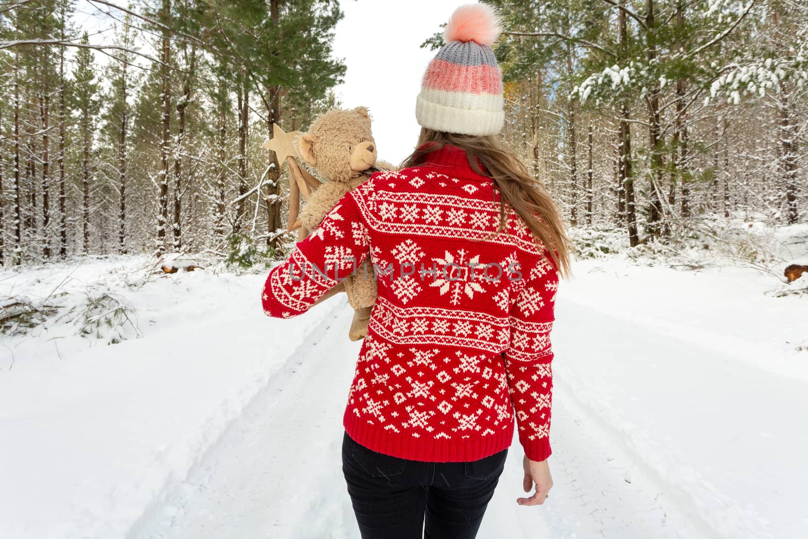 Woman in  snow covered pine plantation forest in winter time.  She is wearing a red and white knitted sweater and wearing a beanie.
